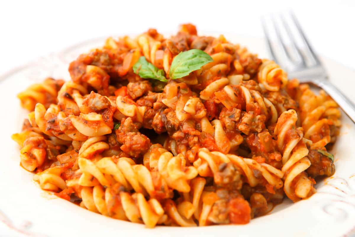 A close up of pasta covered in vegan sauce with a basil leaf on top.