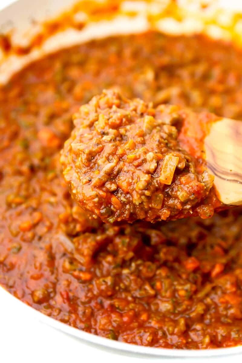 Veggie bolognese sauce in a white pan being stirred with a wooden spoon.