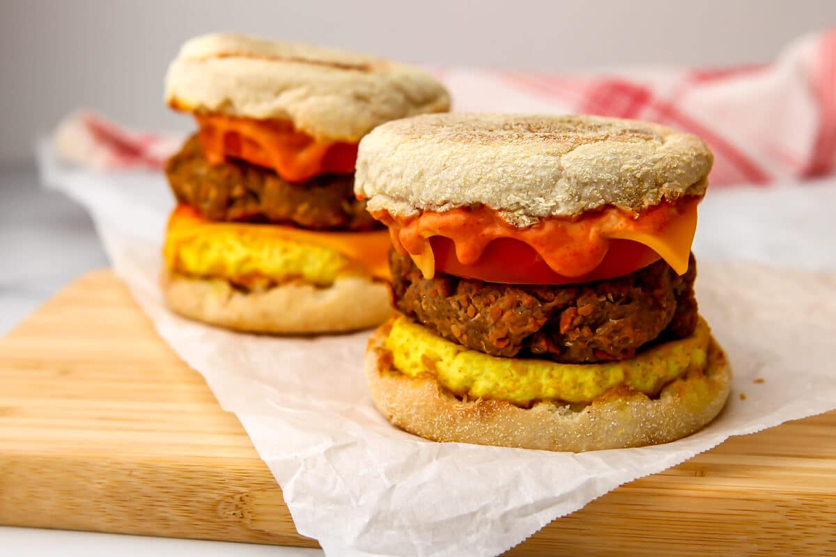 Two vegan egg McMuffins on a cutting board with a red  and white tea towel behind them.