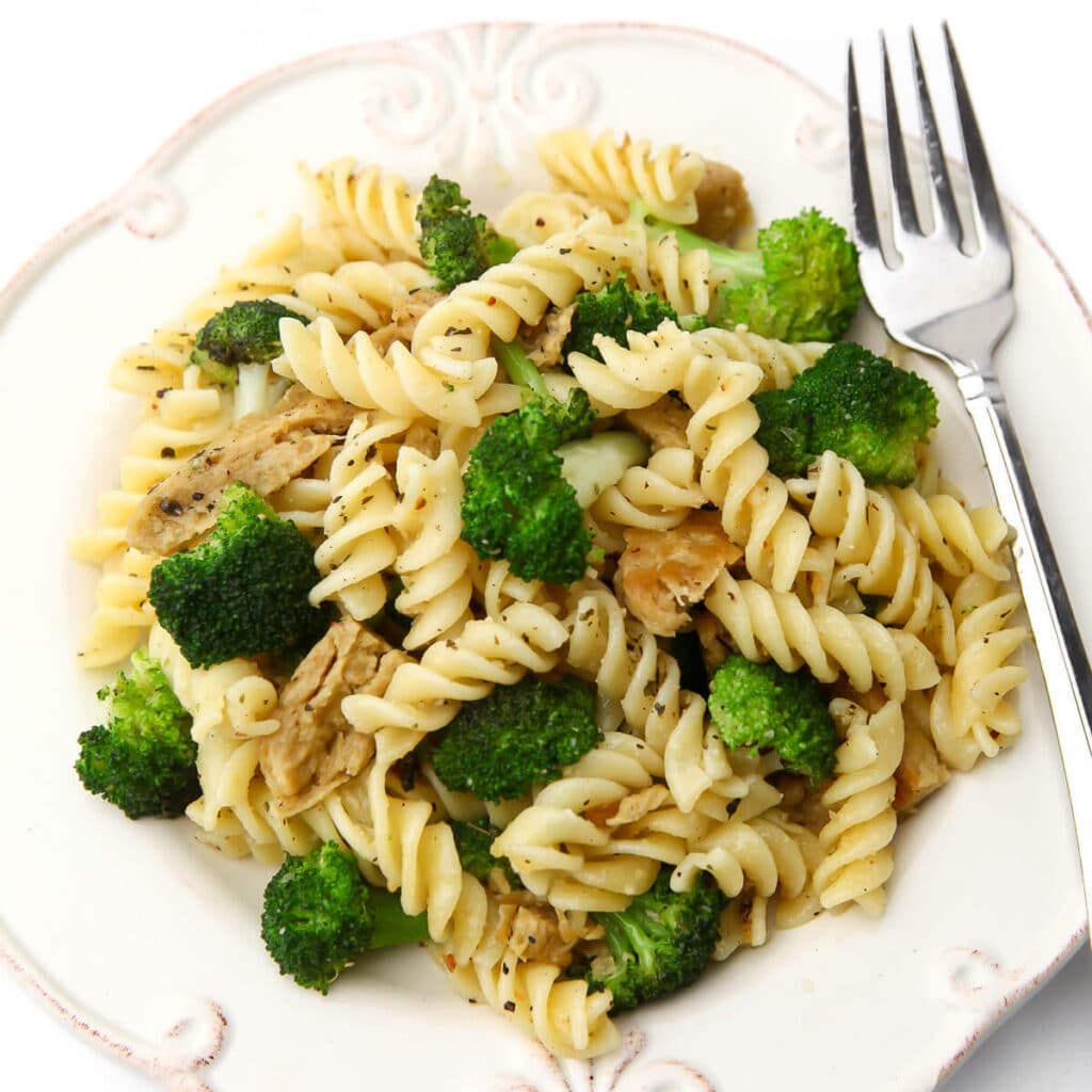 Spiral pasta tossed with broccoli on a white plate.