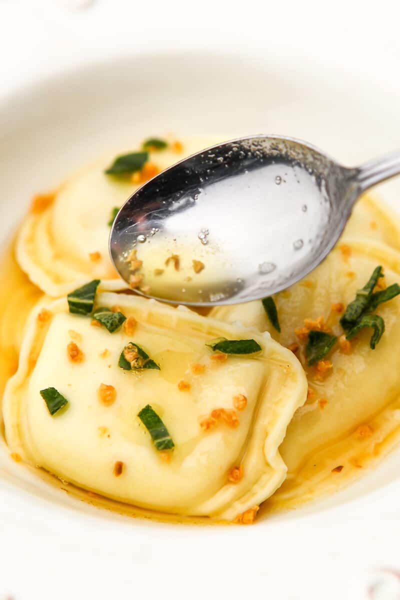 Perogies with vegan brown butter sage sauce being drizzled over them with a spoon.