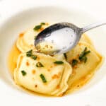 A white bowl with perogies in a brown butter sauce with garlic and sage.