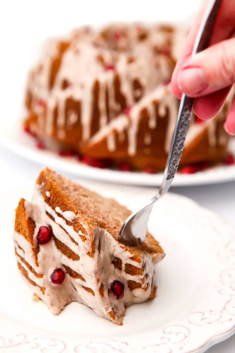 A piece of bundt cake on a white plate with a fork in it with a full cake behind it.