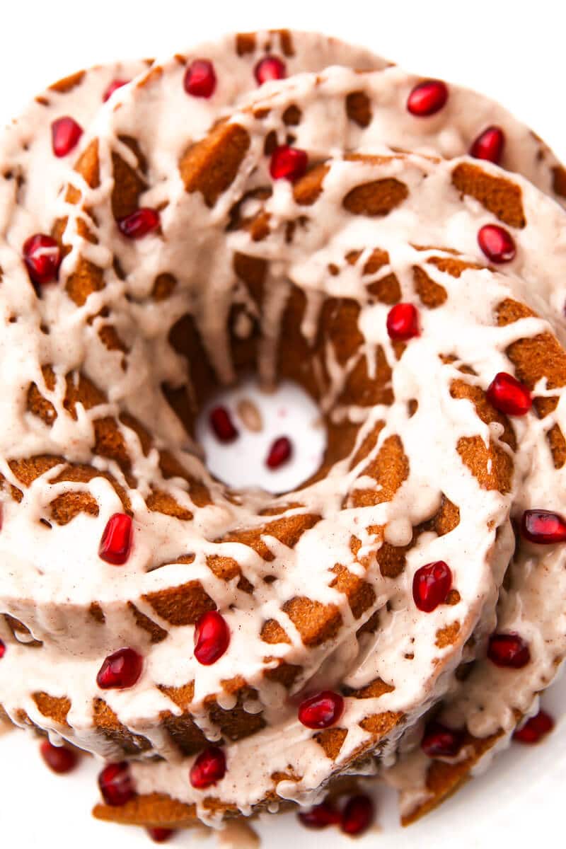 A top view of a bundt cake with vegan icing and pomegranate seeds decorating it.