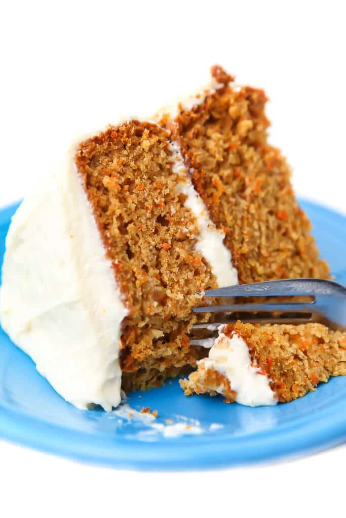 A slice of a vegan carrot cake with vegan cream cheese frosting with a fork cutting off a piece.