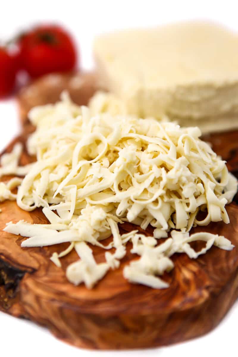 Vegan mozzarella cheese shredded on a wooden cutting board.