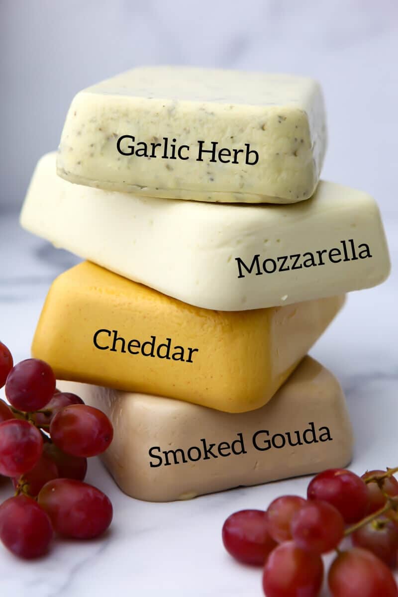A stack of 4 types of vegan cheese that you can easily make including garlic herb, mozzarella, cheddar, and smoked Gouda.