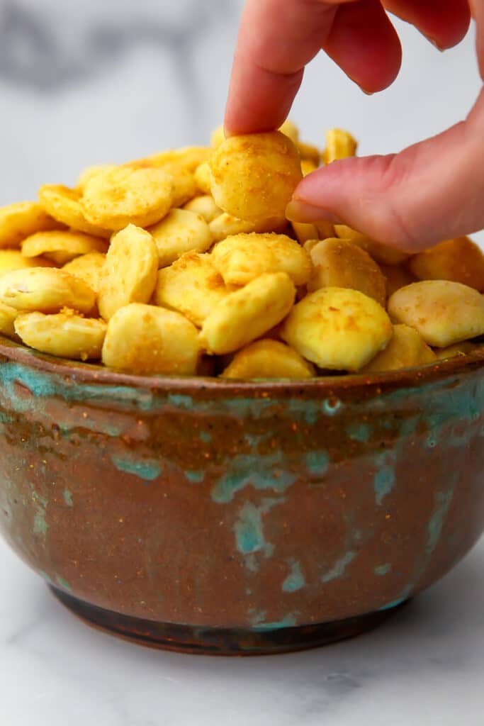 A bowl of vegan cheese flavored crackers with a hand picking one up.