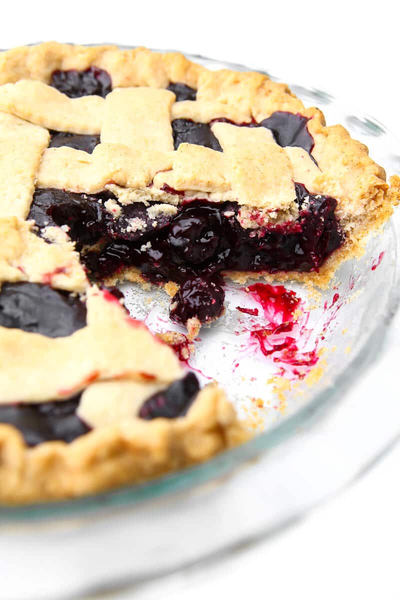 A vegan cherry pie with a lattice top and a piece taken out of it.