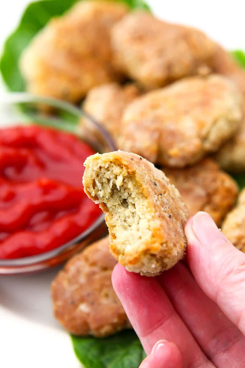 A vegan chicken nugget with a bite out of it being held in someone's hand.