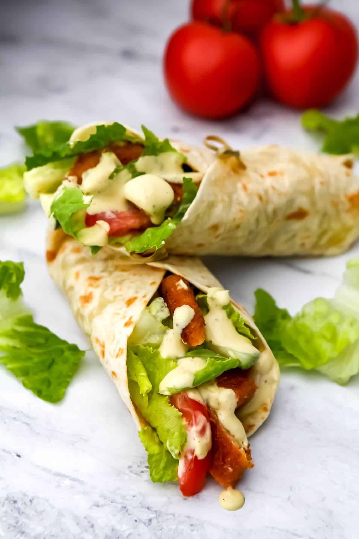 Vegan Caesar chicken wraps on a marble countertop with tomatoes in the background.