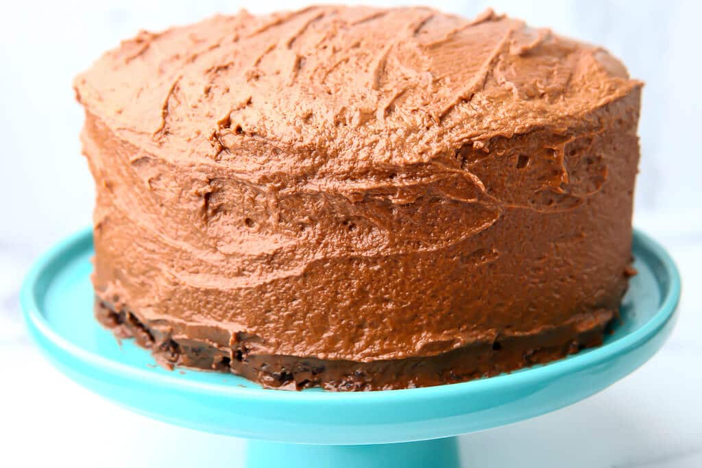 A vegan chocolate cake covered in chocolate buttercream on a blue cake stand.
