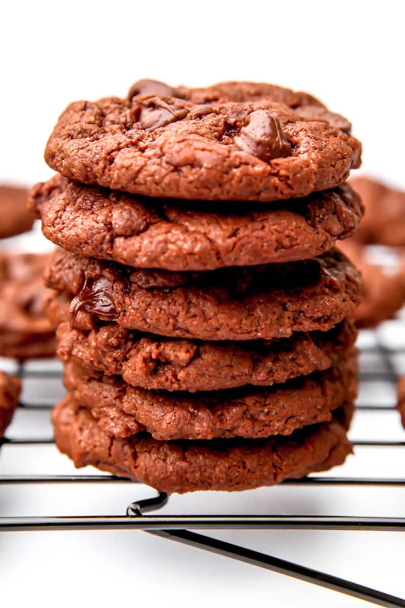A stack of 6 vegan chocolate cookies with chocolate chips on a cooling rack.