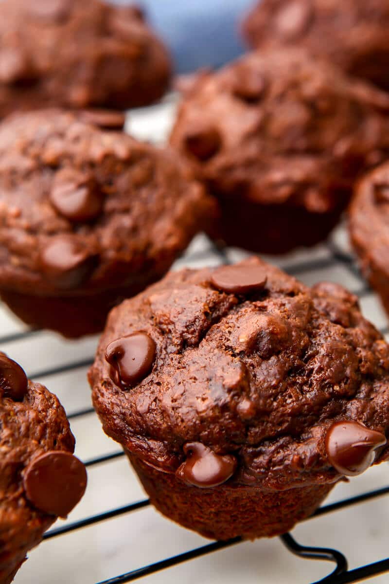 Vegan double chocolate muffins on a cooling wrack with a blue tea towel behind them.