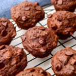 Vegan double chocolate banana muffins on a cooling rack with a blue tea towel behind it.