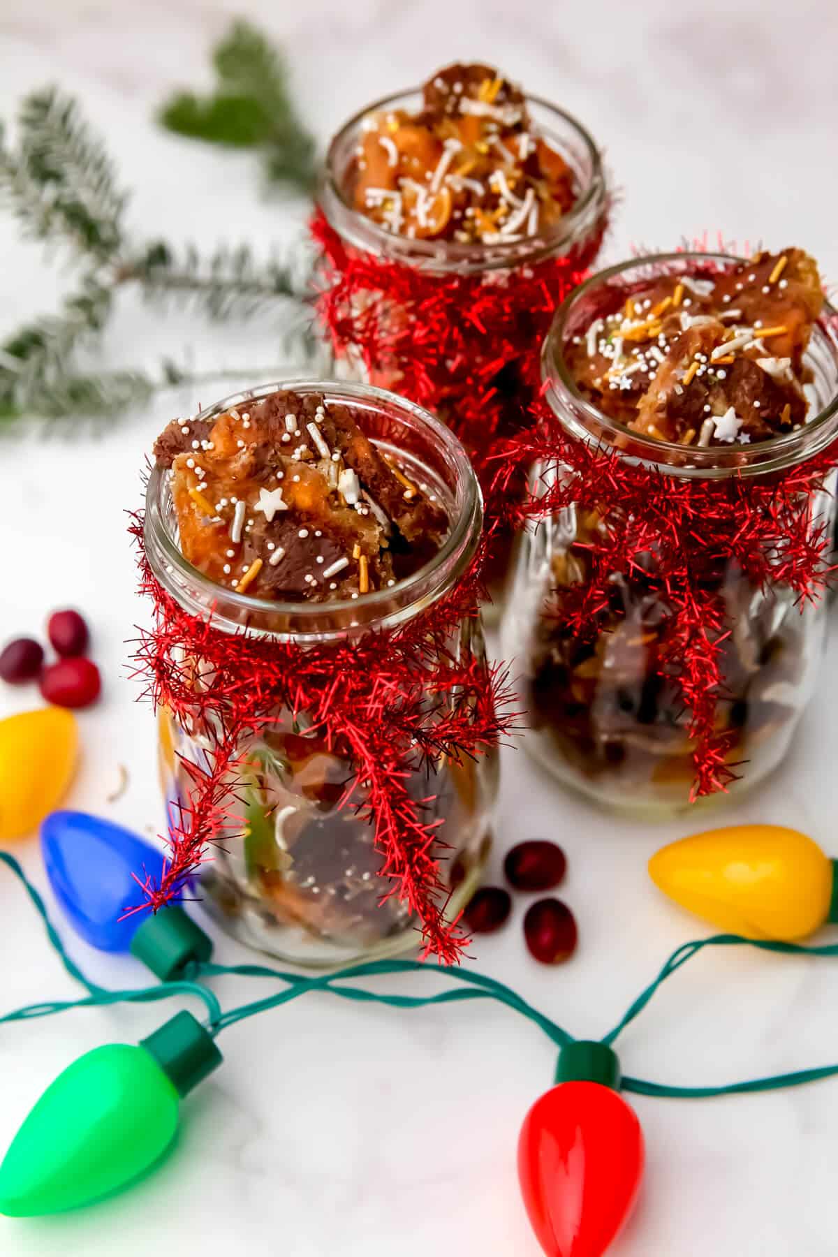 Vegan Christmas crack in jars with a pine bow behind them and Christmas lights in frount.i