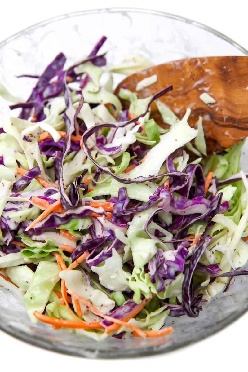 A bowl of shredded cabbage with dressing being stirred in to make vegan coleslaw.
