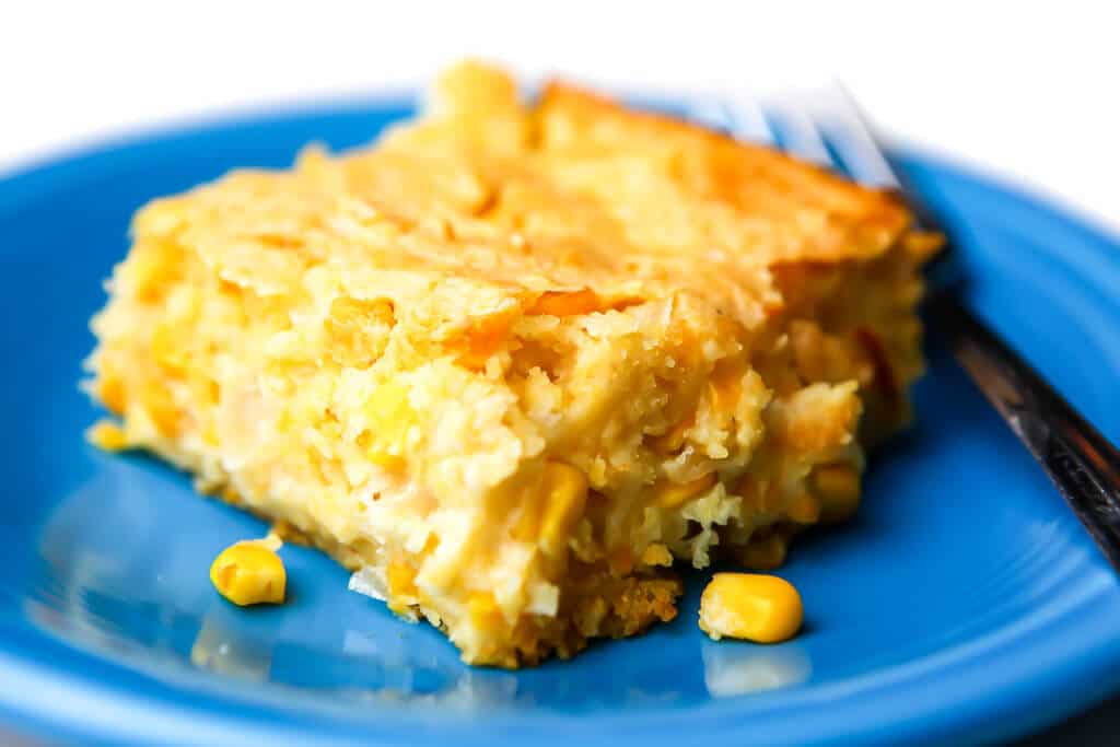 A slice of vegan corn bread casserole on a blue plate with a fork on the side.