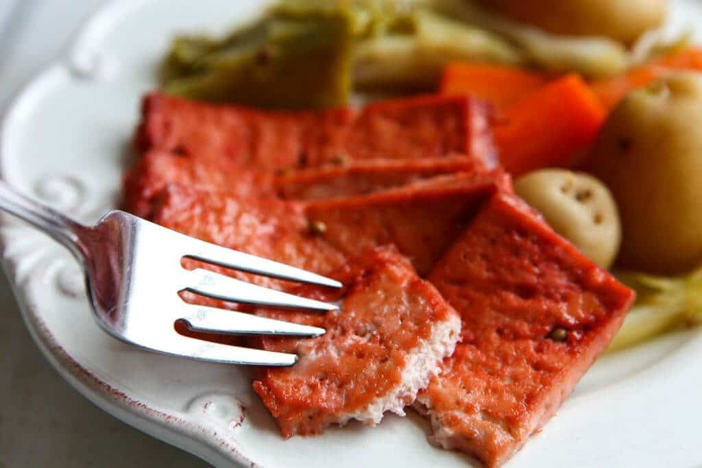 Vegan corned beef made with tofu on a white plate with potatoes, carrots, and cabbage.