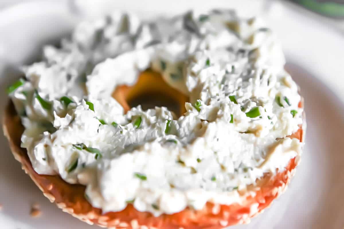 Vegan cream cheese with chives spread on a toasted bagel.