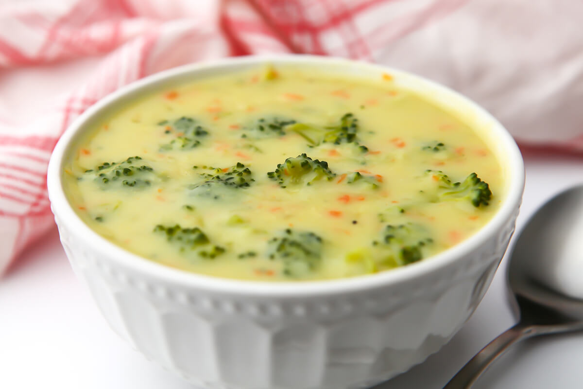 A bowl of vegan cream of broccoli soup with a red and white tea towel behind it.