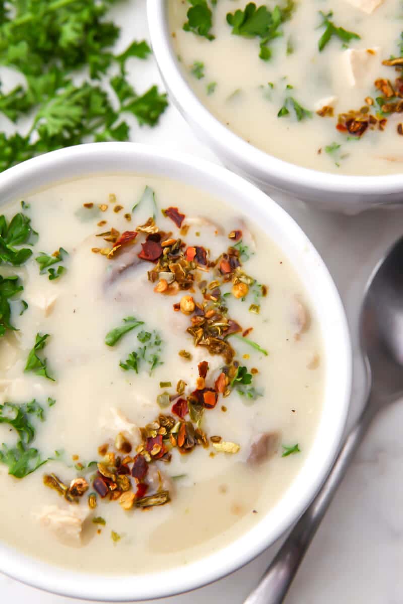 A top view of two bowl of vegan cream of chicken soup with parsley and a spoon on the side.