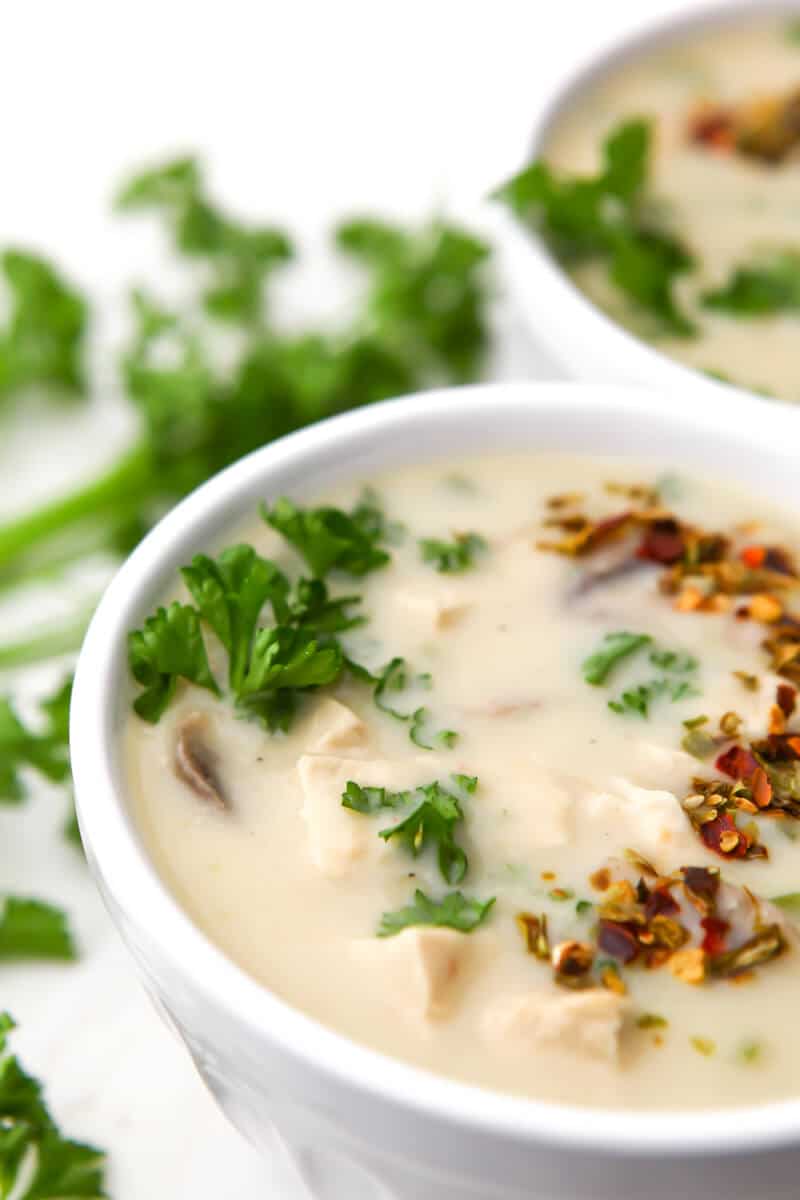 Two white bowls filled with vegan cream of chicken soup and topped with parsley with more parsley on the side.