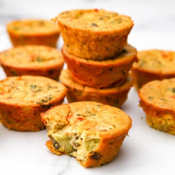 Vegan egg muffins filled with veggies stacked on a marble counter top.