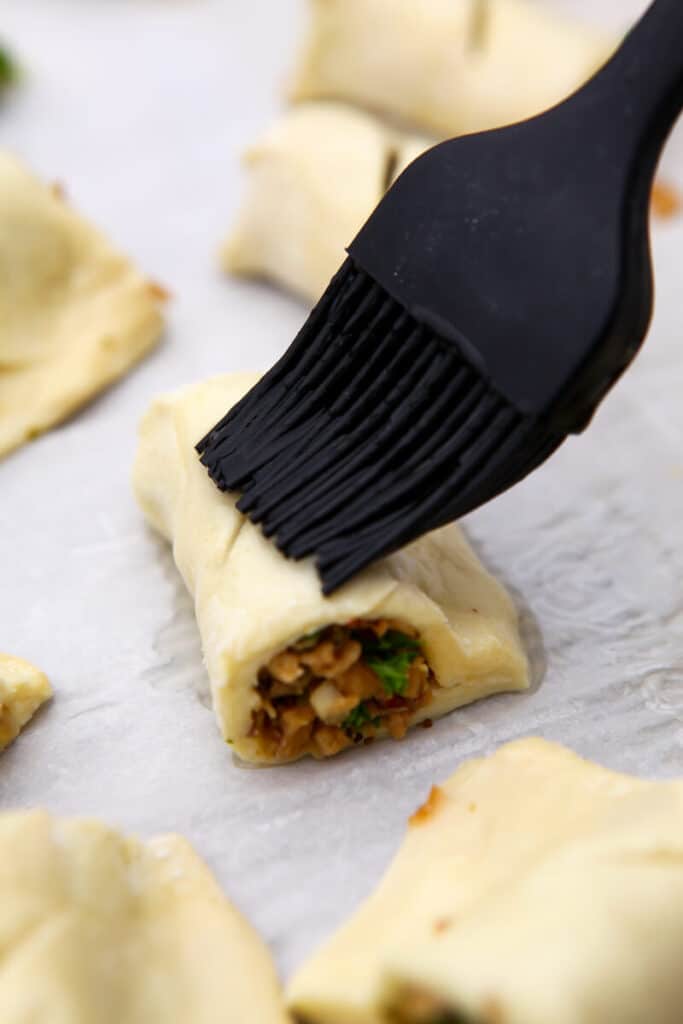 A vegan sausage roll being brushed with a vegan egg wash.