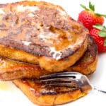 A stack of vegan French toast on a white plate with strawberries on the side.