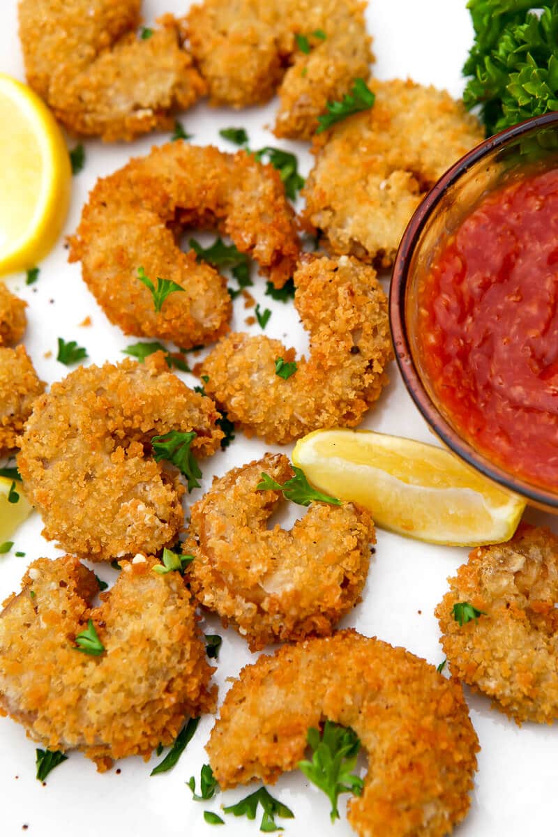 A top view of a plate of vegan fried shrimp on a white plate with cocktail sauce on the side.