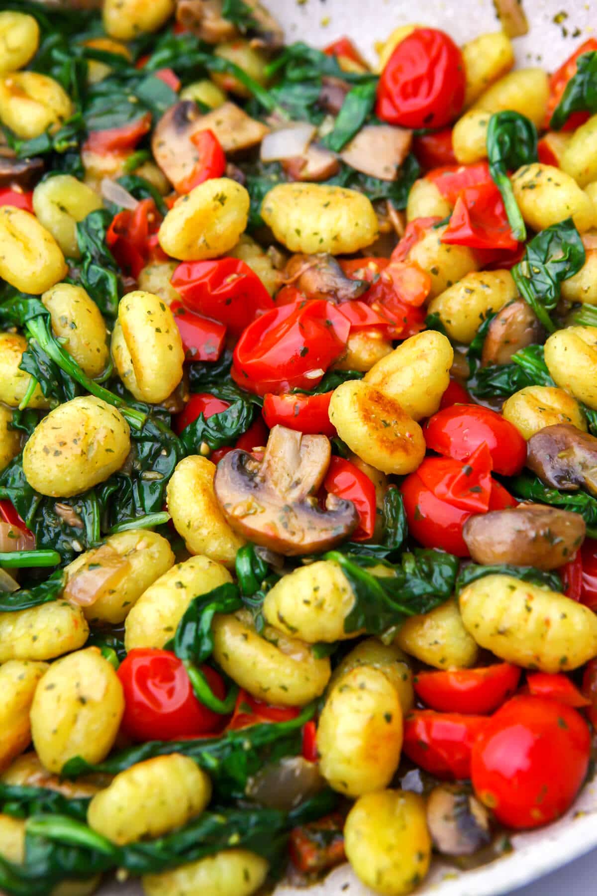 A close up of gnocchi with veggies and pesto in a frying pan.