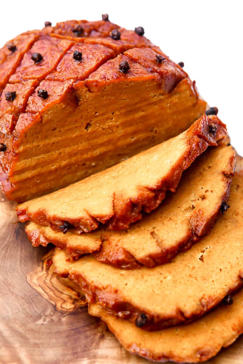 A top view of a vegan ham cut into slices on a wooden cutting board.