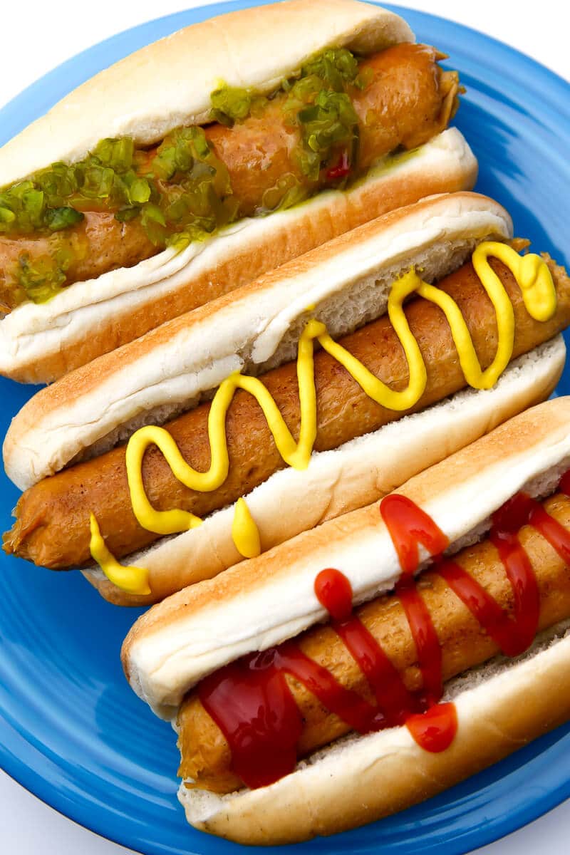A top view of three veggie hot dogs in hot dog buns on a blue plate.