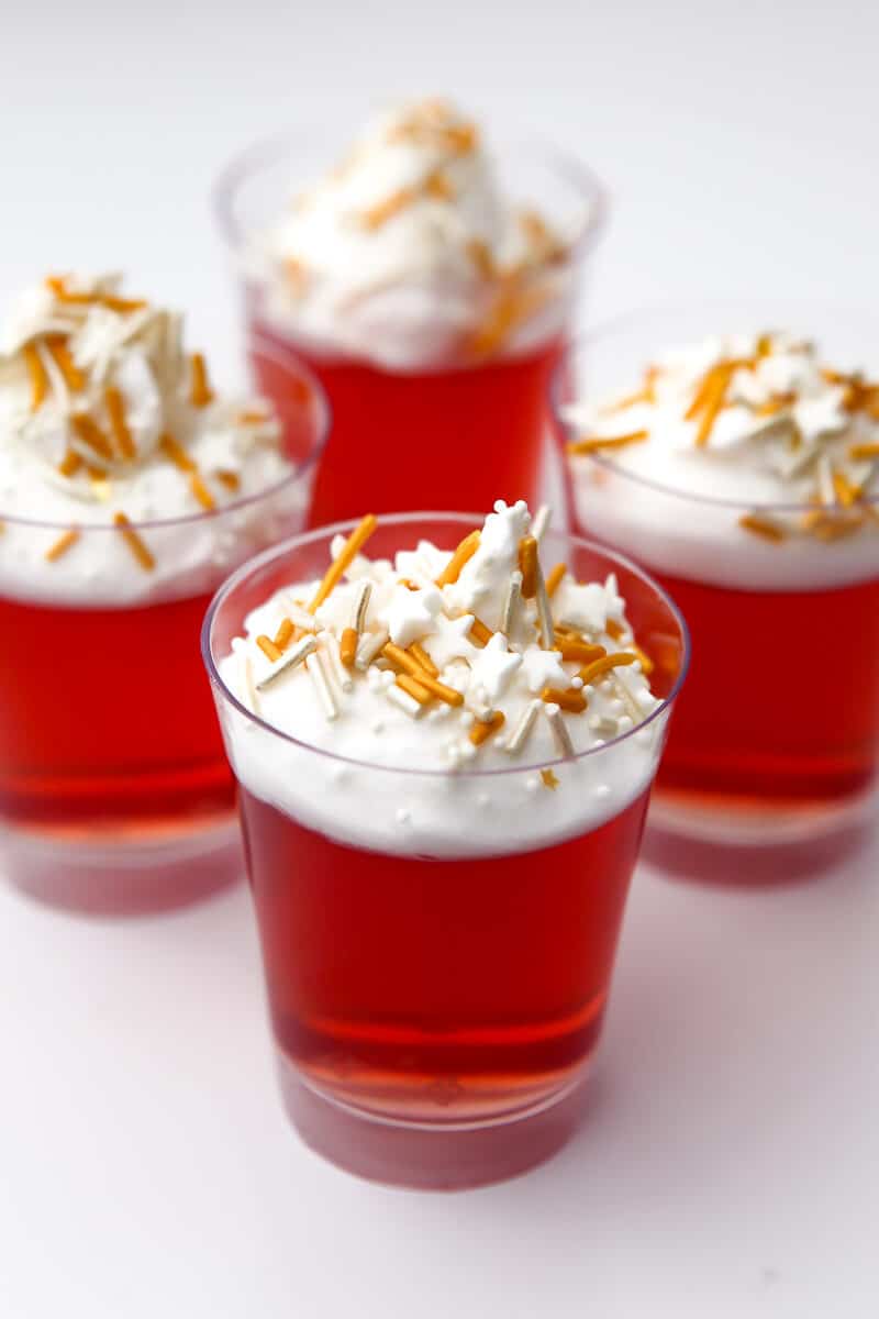 Four jello shots with vegan whipped cream and sprinkles on top.