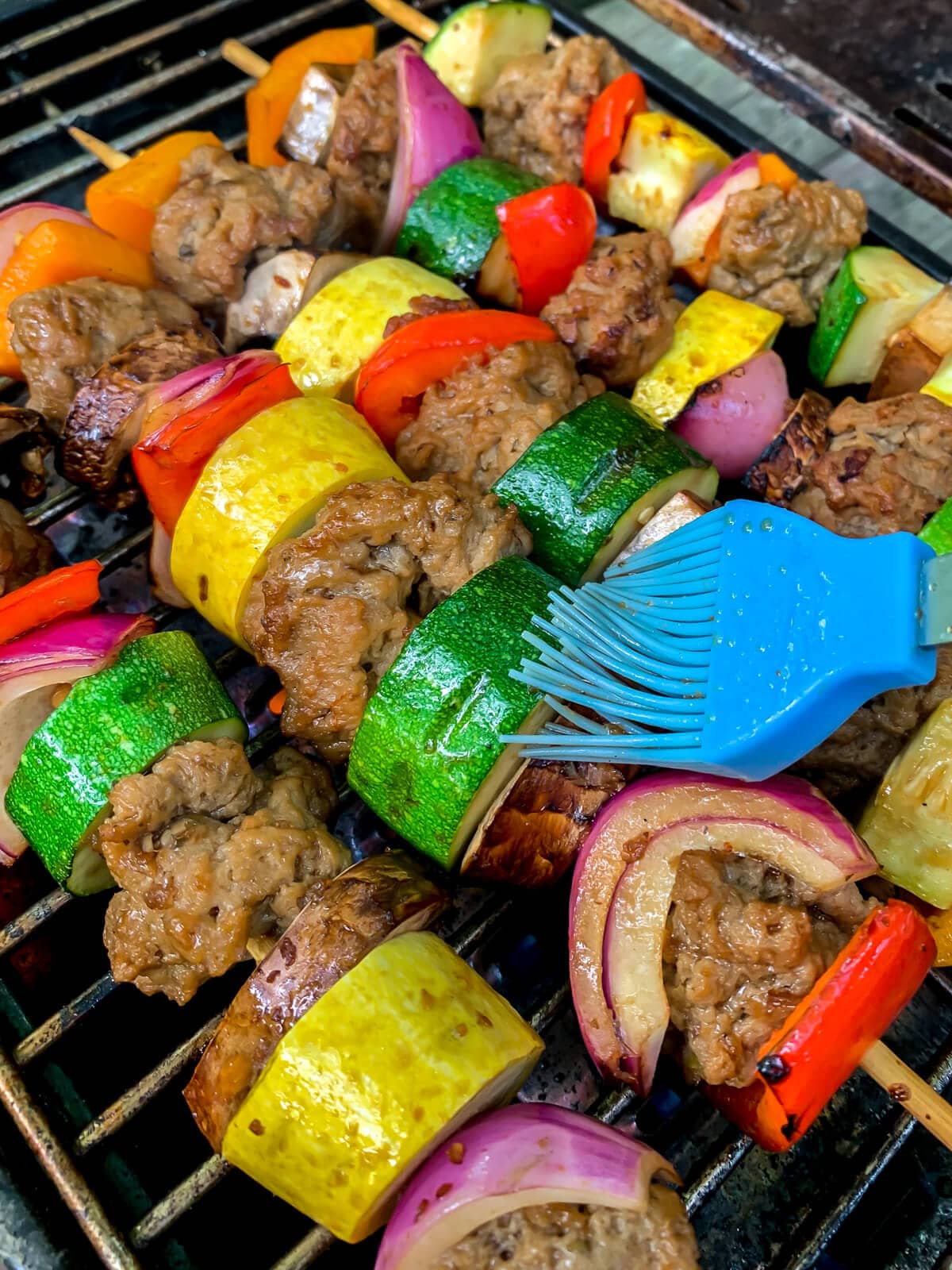 Seitan kebabs being brushed with teriyaki sauce on a grill.