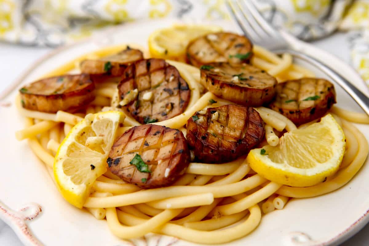 King oyster mushroom scallops served over a bed of pasta with lemon wedges on the side.