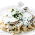 A white plate filled with linguine topped with vegan scallops and a garlic cream sauce garnished with parsley.