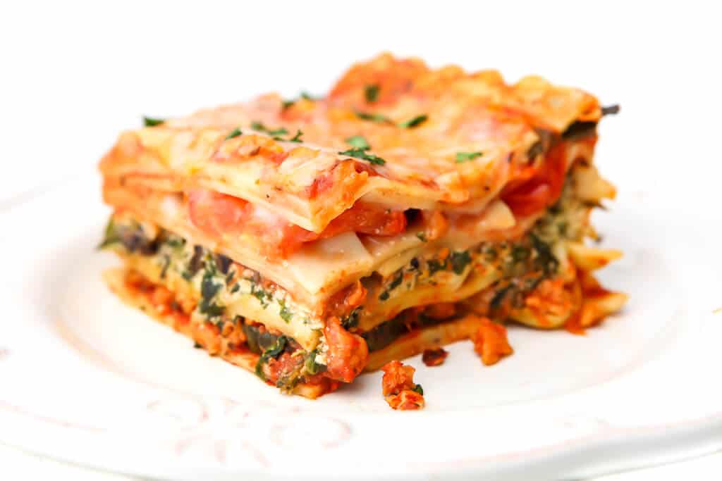 A piece of vegetarian lasagna with layers of tofu ricotta, spinach, tomatoes and vegan cheese.