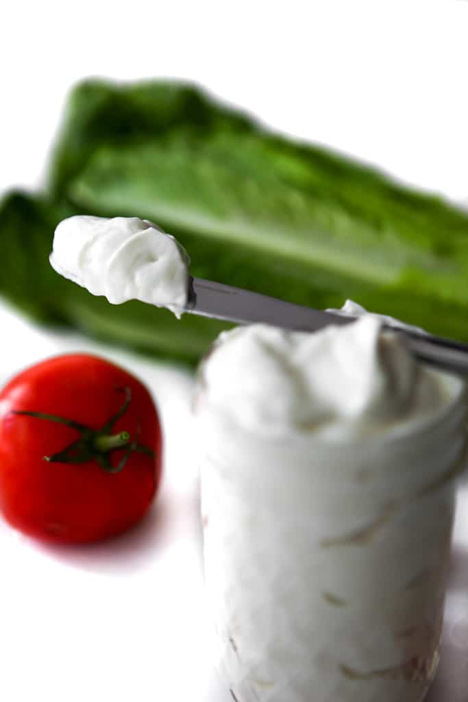 Vegan mayo on a knife with veggies behind it.