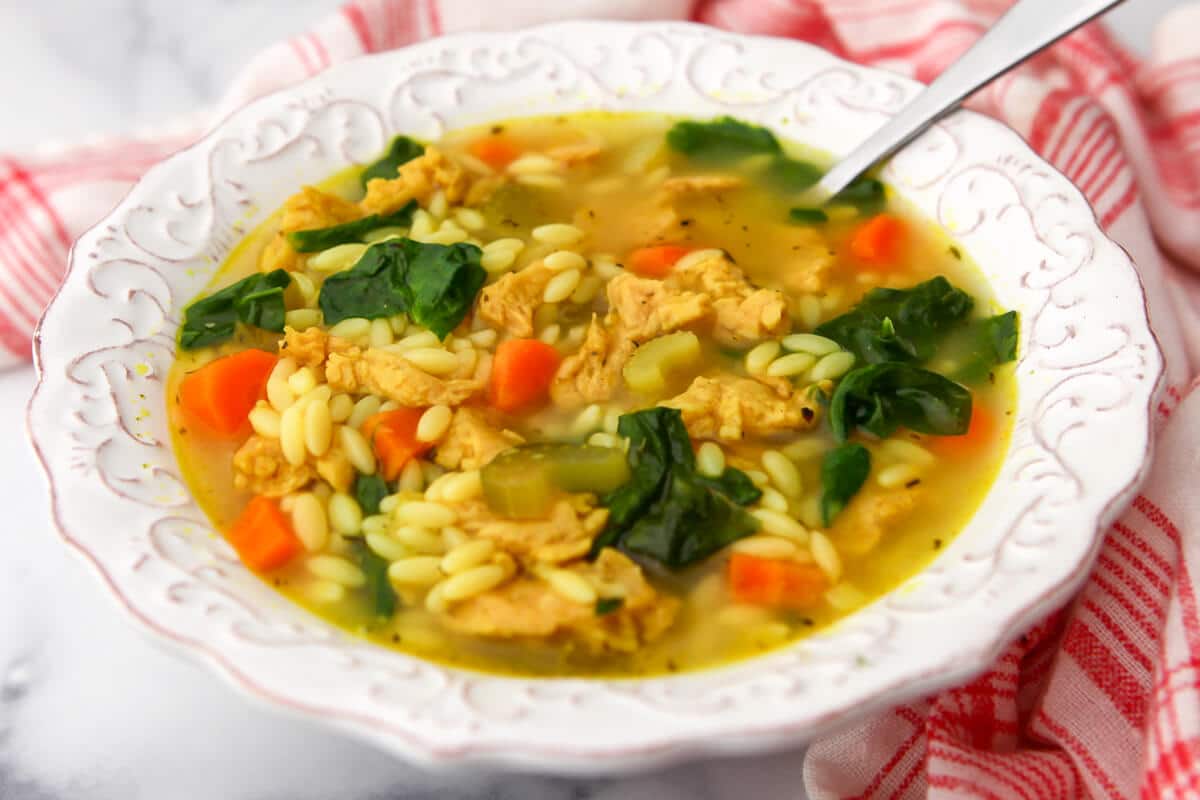 A white bowl filled with vegan orzo soup with carrots, celery, vegan chicken, and spinach.