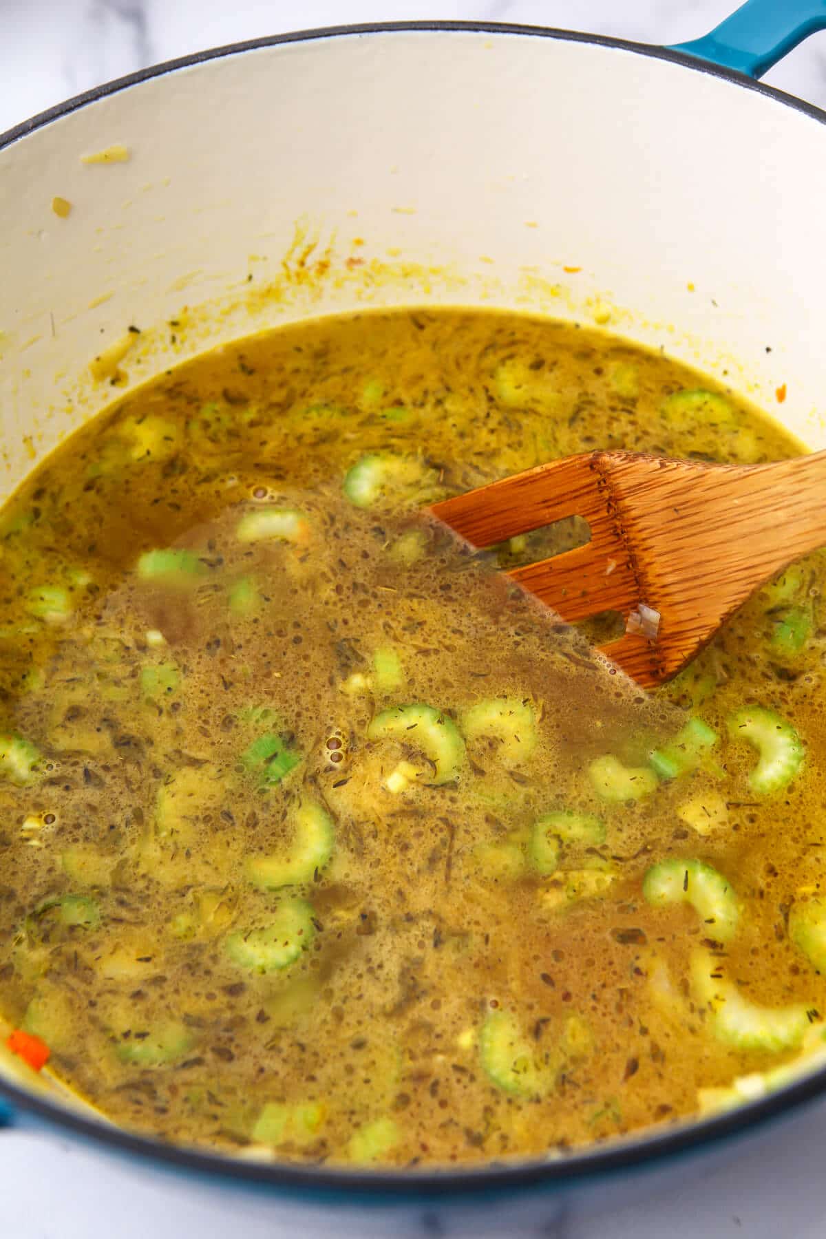 Vegetables and broth simmering in a large soup pot before adding vegan chicken and orzo.