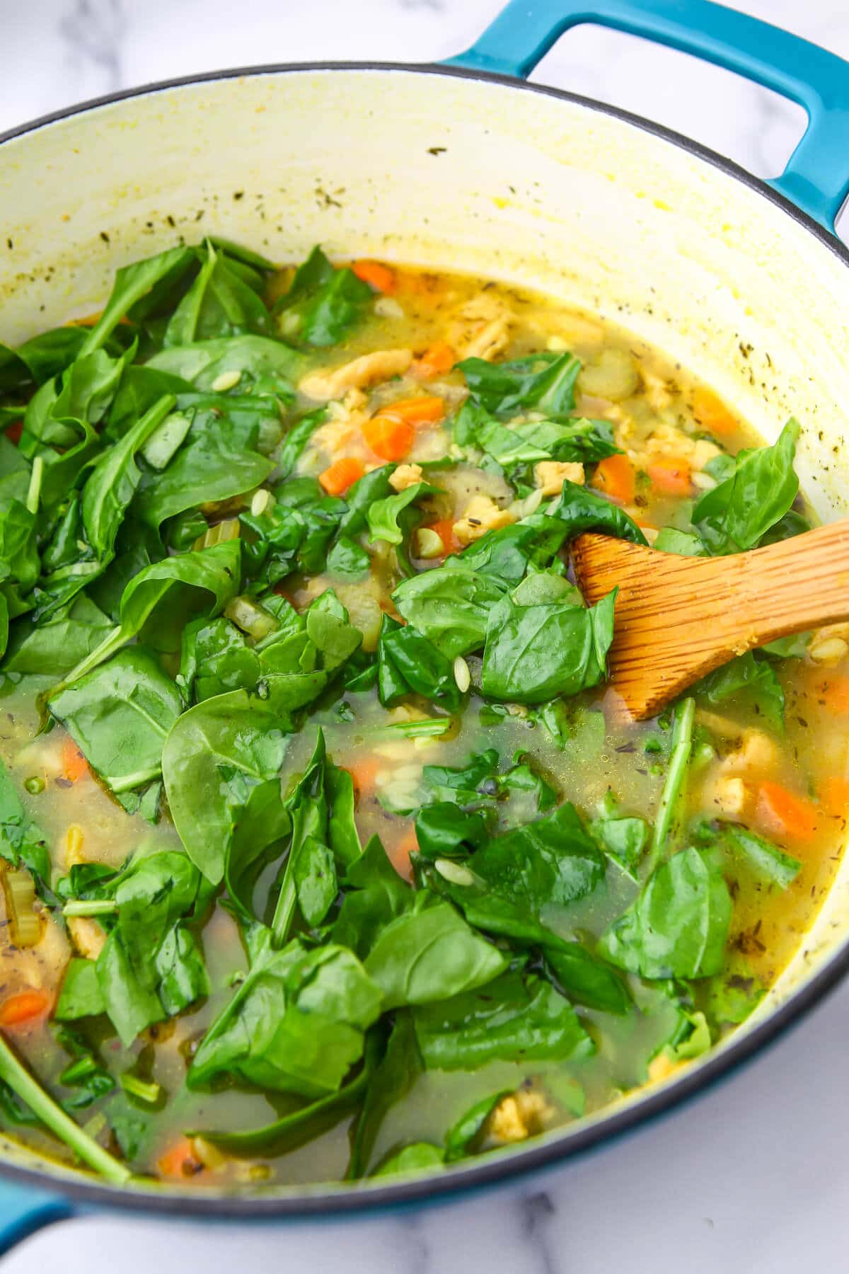 Spinach being added at the end of making vegan orzo soup.