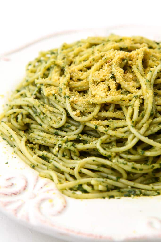 A white plate filled with spaghetti tossed in pesto and topped with vegan Parmesan cheese.