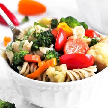 A bowl of easy vegan pasta primavera with broccoli, carrots, cauliflower, and tomatoes.