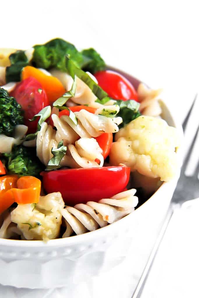 A bowl filled with gluten free vegan pasta primavera made with carrots, peppers, broccoli, cauliflower, and tomatoes.