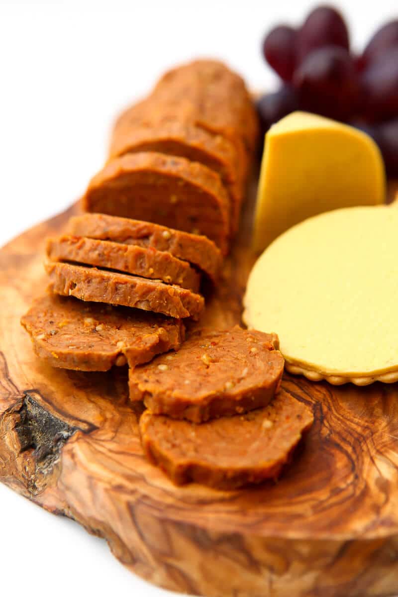 Vegan pepperoni on a wooden cutting board cut into slices with vegan cheddar next to it.