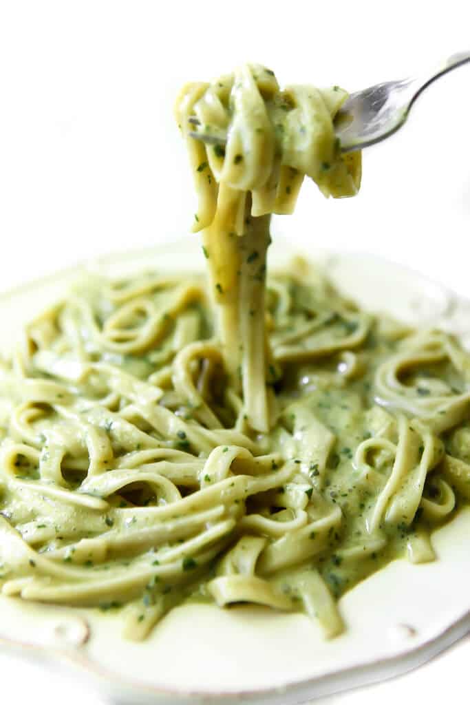 A plate filled with creamy pesto sauce over pasta and a fork full of the pasta over the dish.