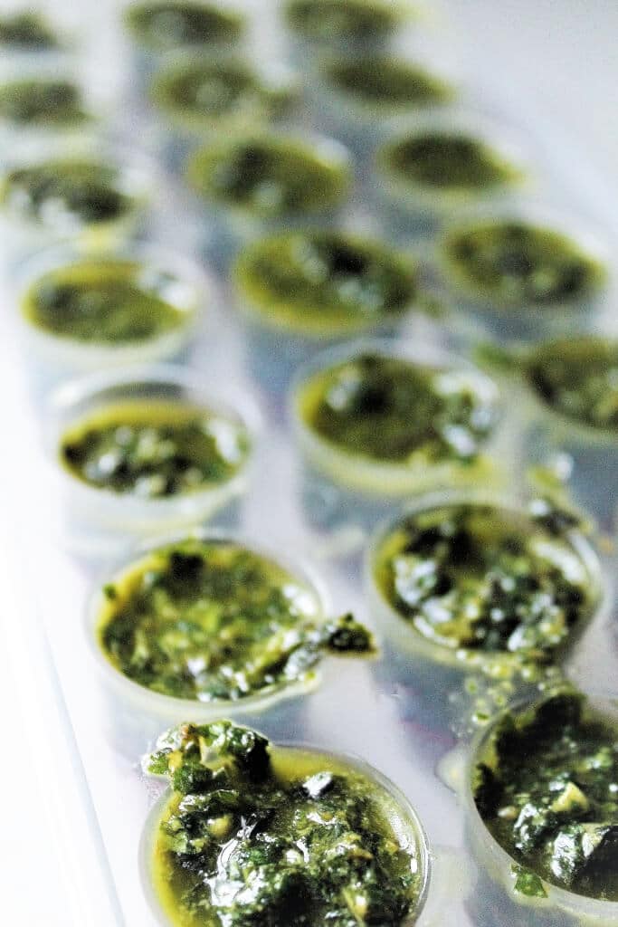 An ice cube tray filled with an easy pesto recipe ready to freeze into cube to be used later. 