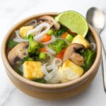 A brown bowl filled with vegan Pho soup with a wedge of lime on the side of the bowl.